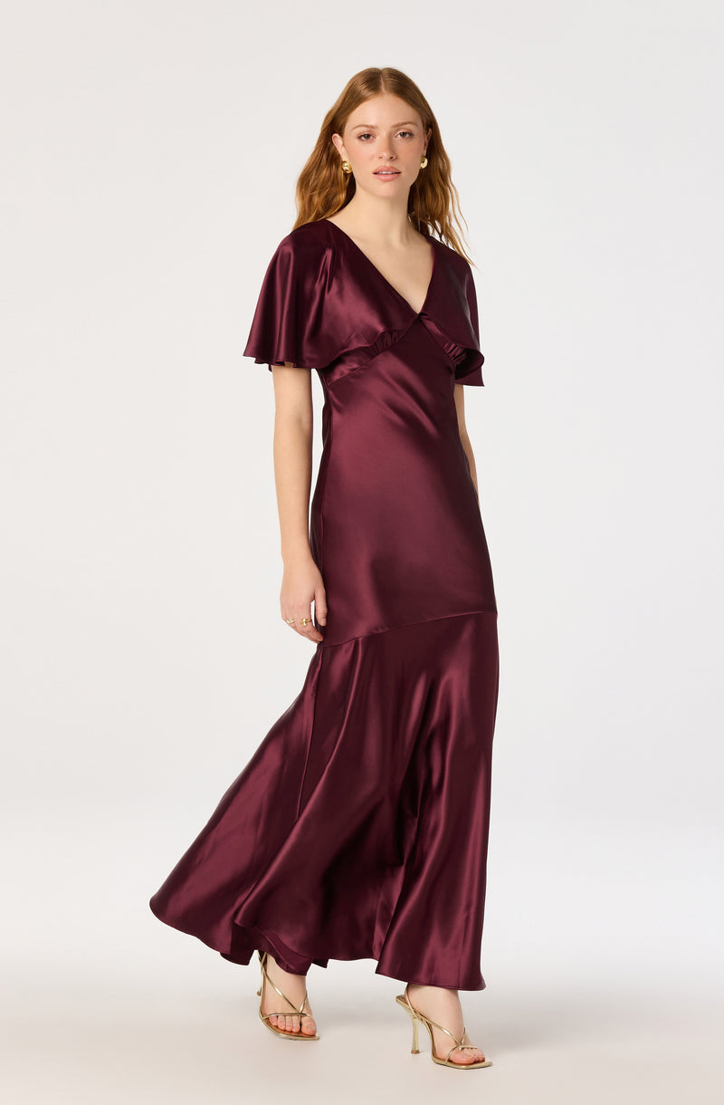 Woman in a burgundy satin gown with ruffled short sleeves and a flowing skirt.
