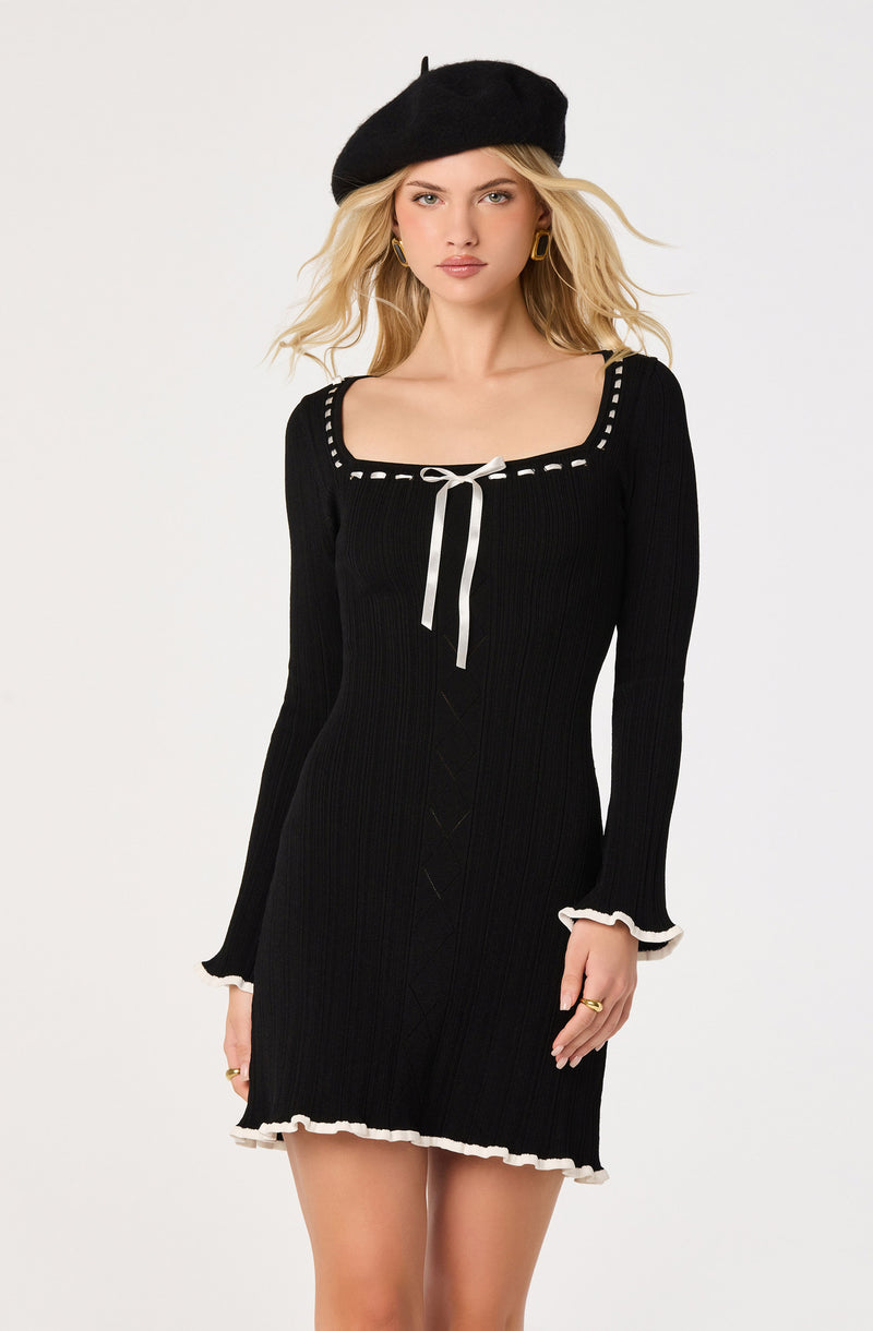 Woman in black ribbed dress with white trim, black beret, and gold hoop earrings.