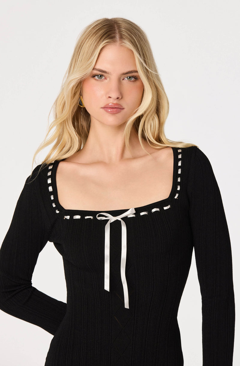 Woman in black ribbed long-sleeve top with square neckline, white trim, and bow detail.