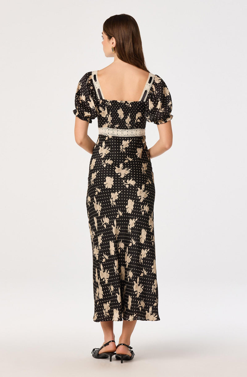Woman in a black and beige floral and polka dot printed dress with puffed short sleeves.