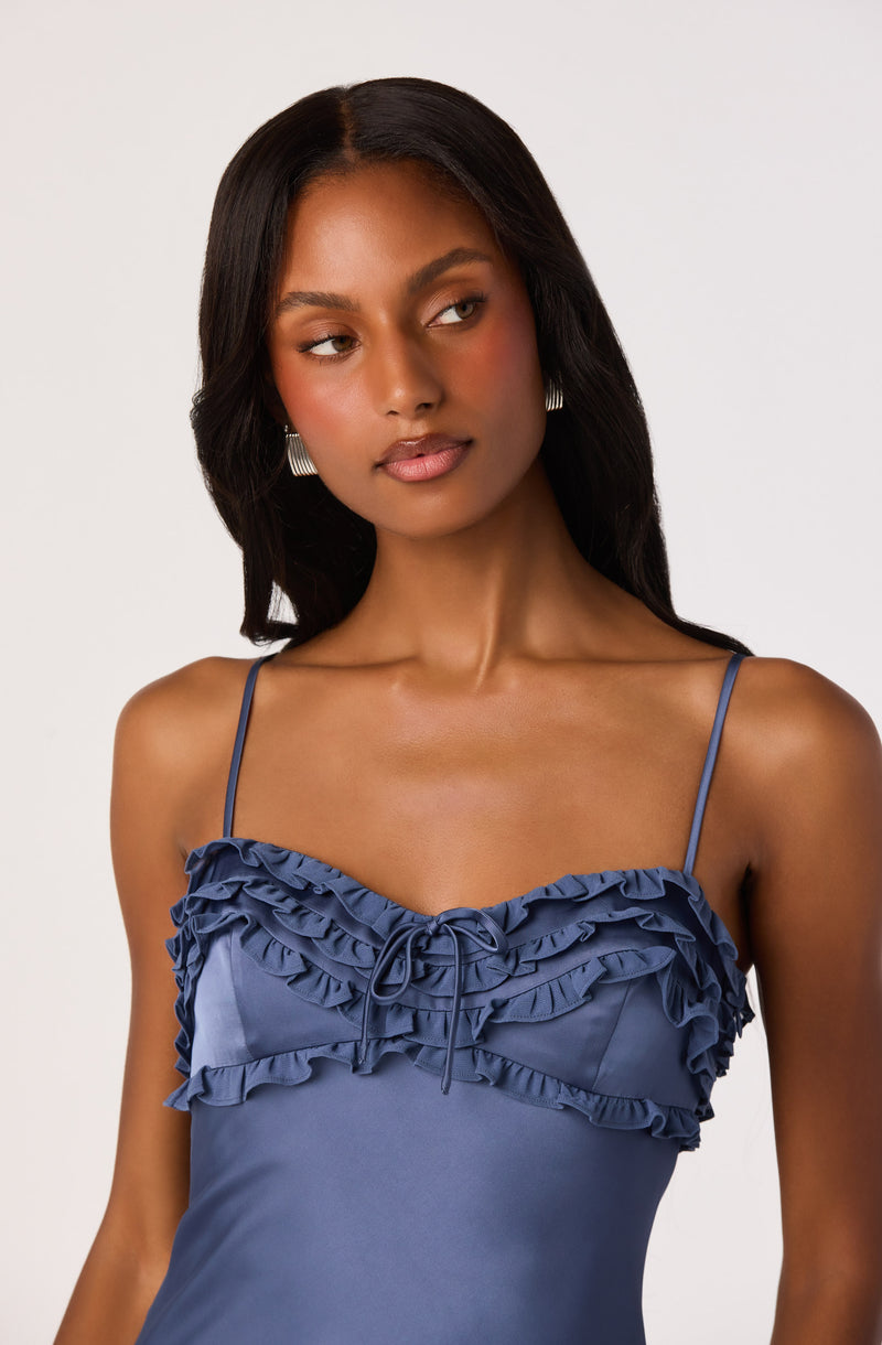 Woman wearing a blue satin dress with ruffled details and spaghetti straps.