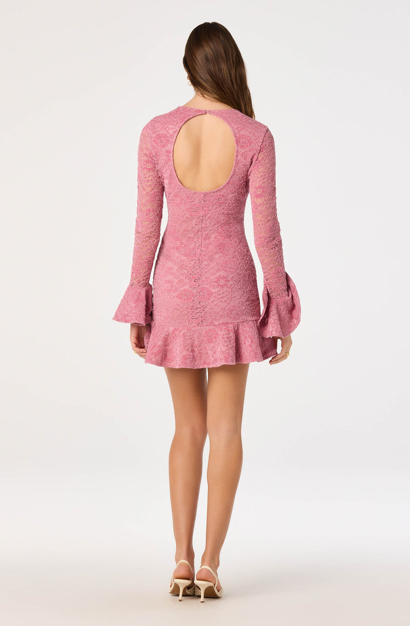 Back view of a woman wearing a pink textured dress with long sleeves, flared cuffs, and a ruffled hem.