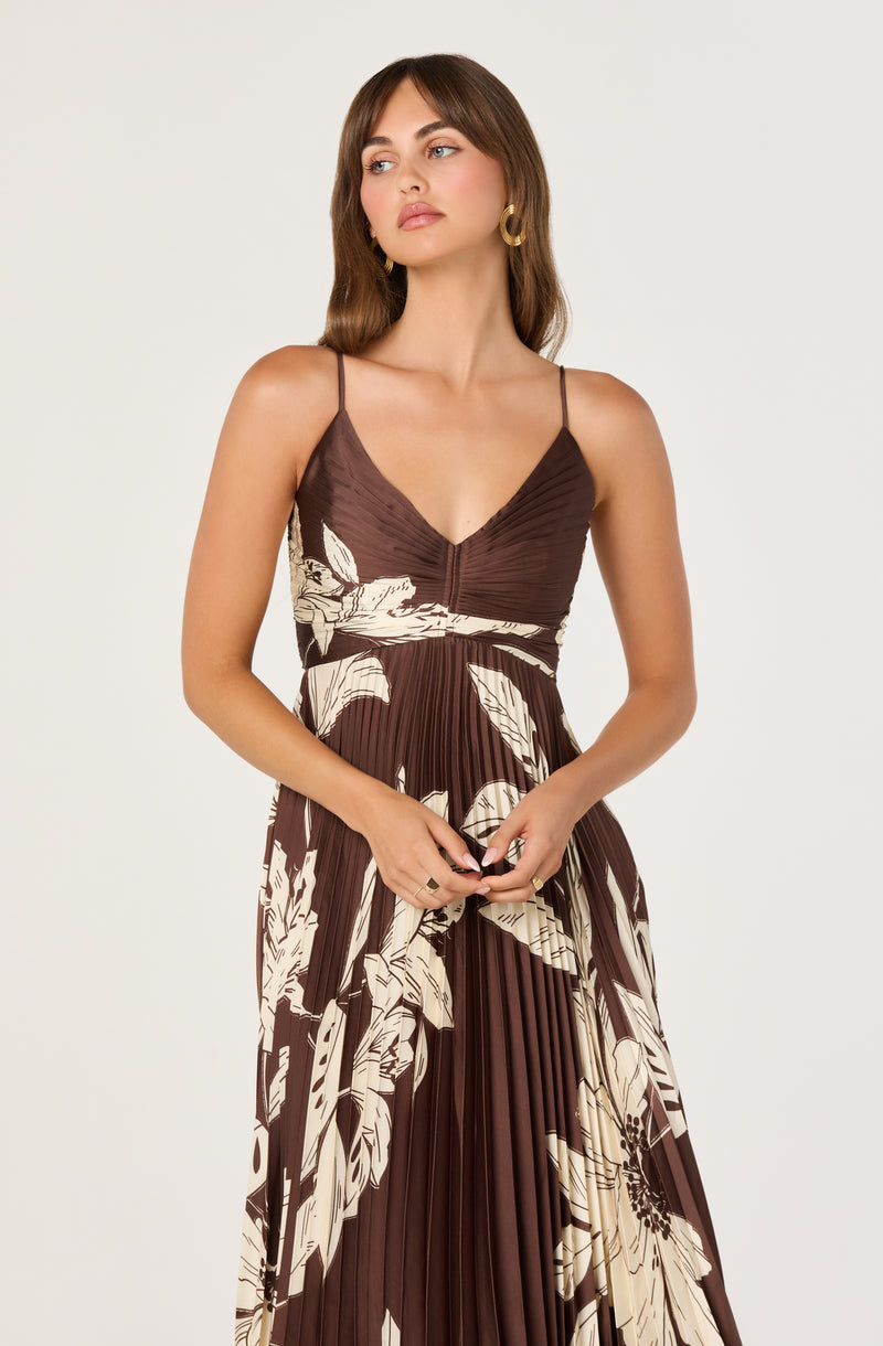 Girl in a brown and cream floral pleated dress with spaghetti straps and gold hoop earrings.