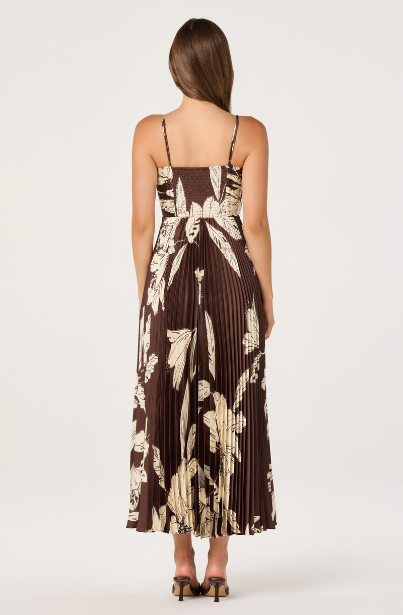 Back view of a woman wearing a sleeveless, floral-patterned, pleated maxi dress with thin straps.