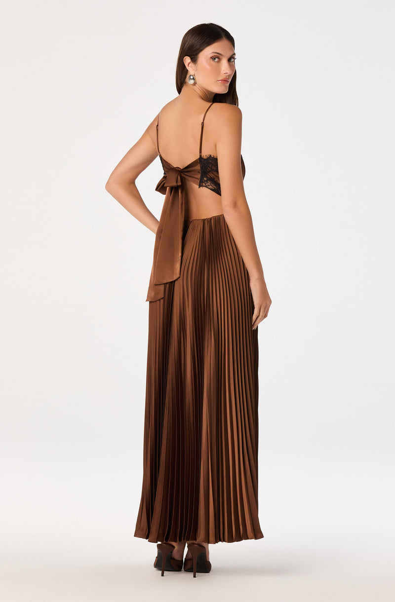 Woman wearing a brown satin pleated skirt and a brown satin top with black lace details and thin straps.