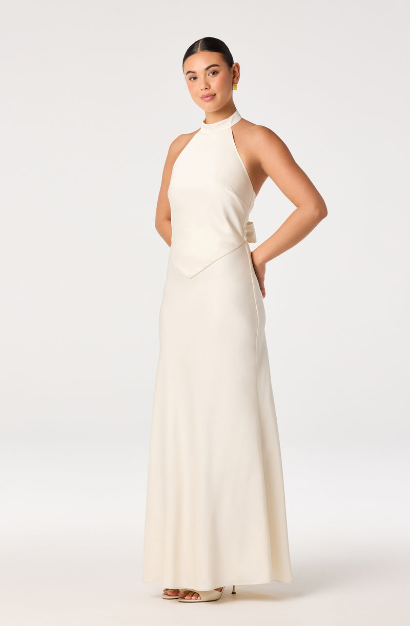 Woman wearing a sleeveless, high-neck cream-colored gown with a fitted waist and floor-length skirt.