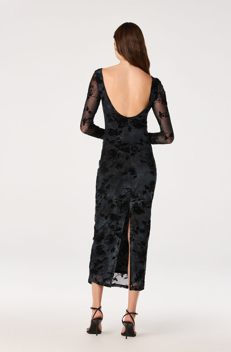 Woman in a black velvet dress with floral lace pattern, deep back, and slit at the bottom.