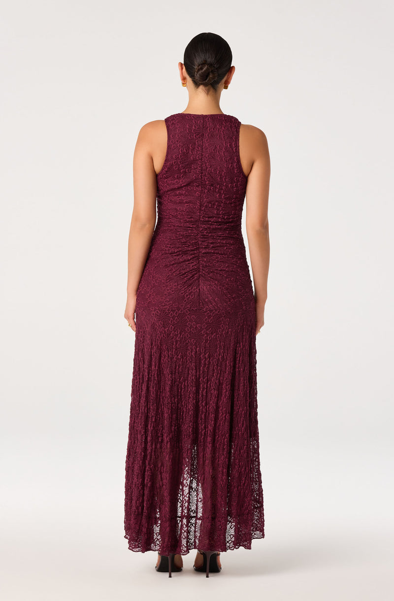 Back view of a woman in a sleeveless, burgundy lace gown with a knit pattern, fitted at the waist and flowing to the floor.