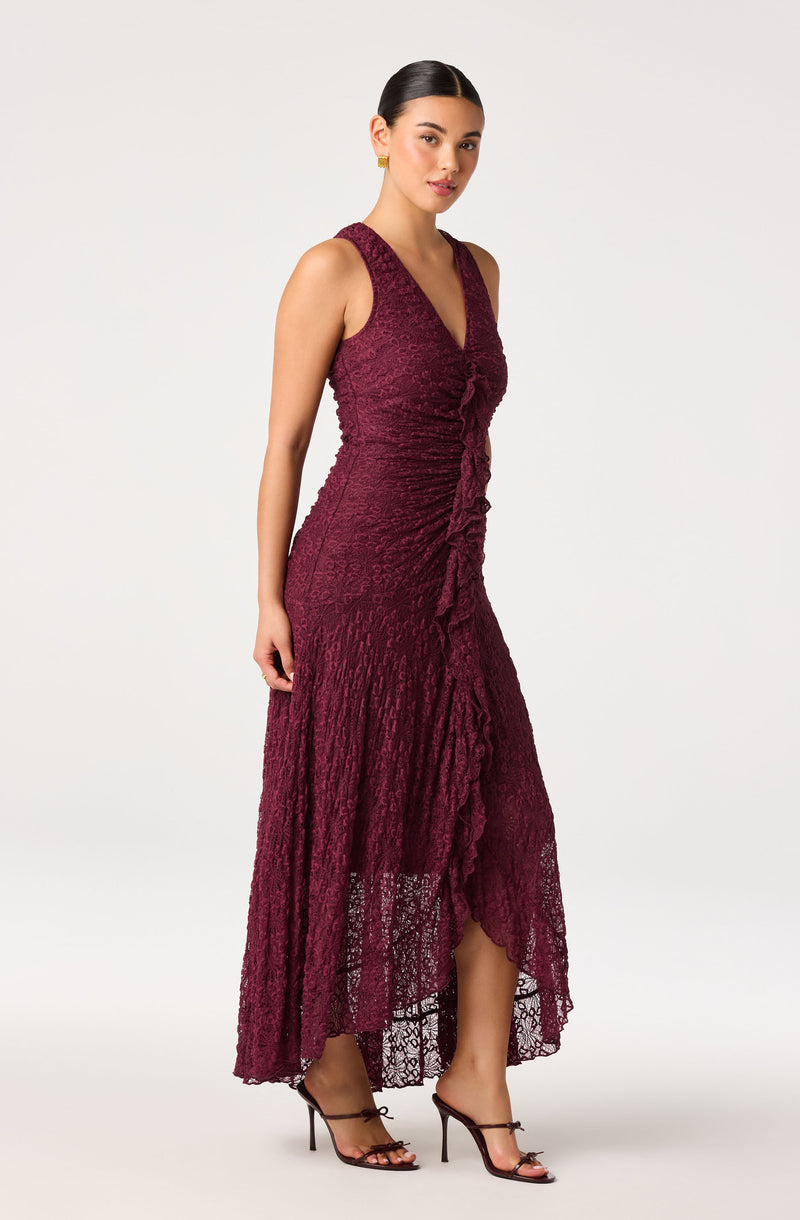 Woman wearing a sleeveless, deep v-neck, burgundy lace dress with ruffled front and high-low hem.