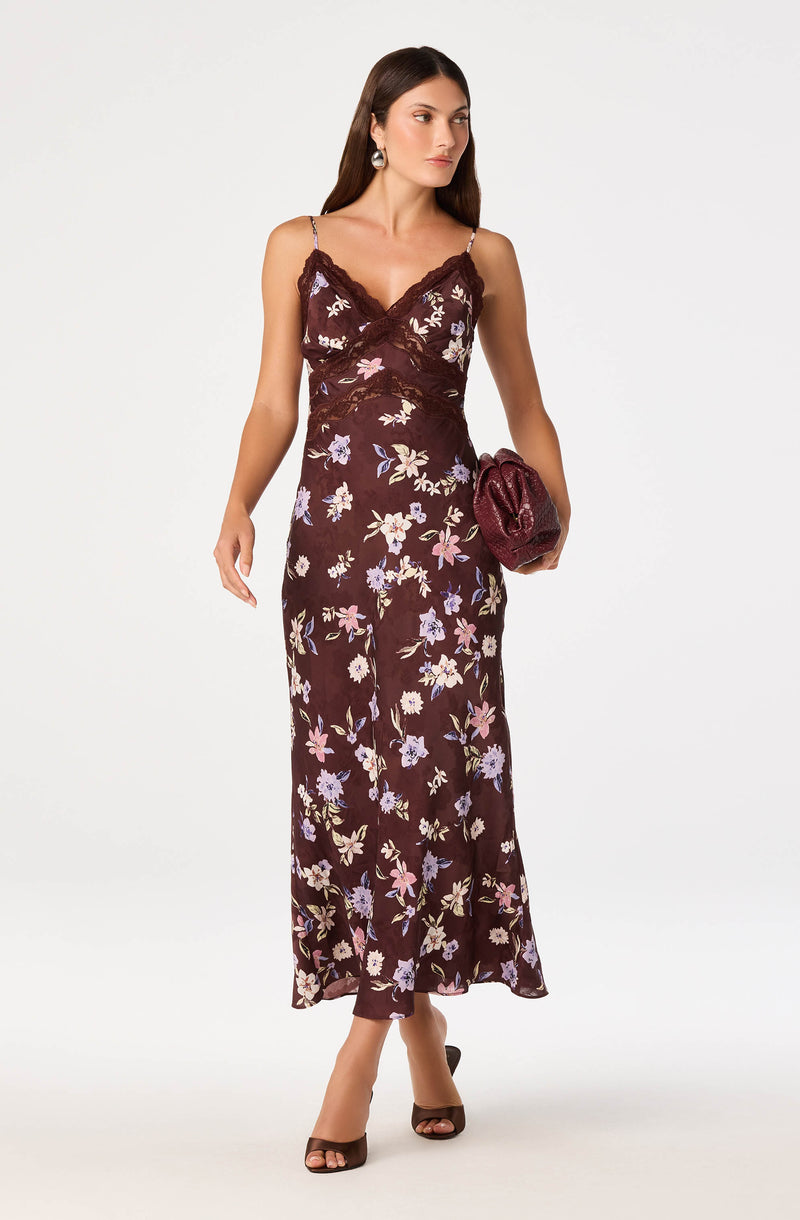 Woman wearing a dark floral sleeveless dress with lace details, carrying a maroon clutch, and wearing heels.