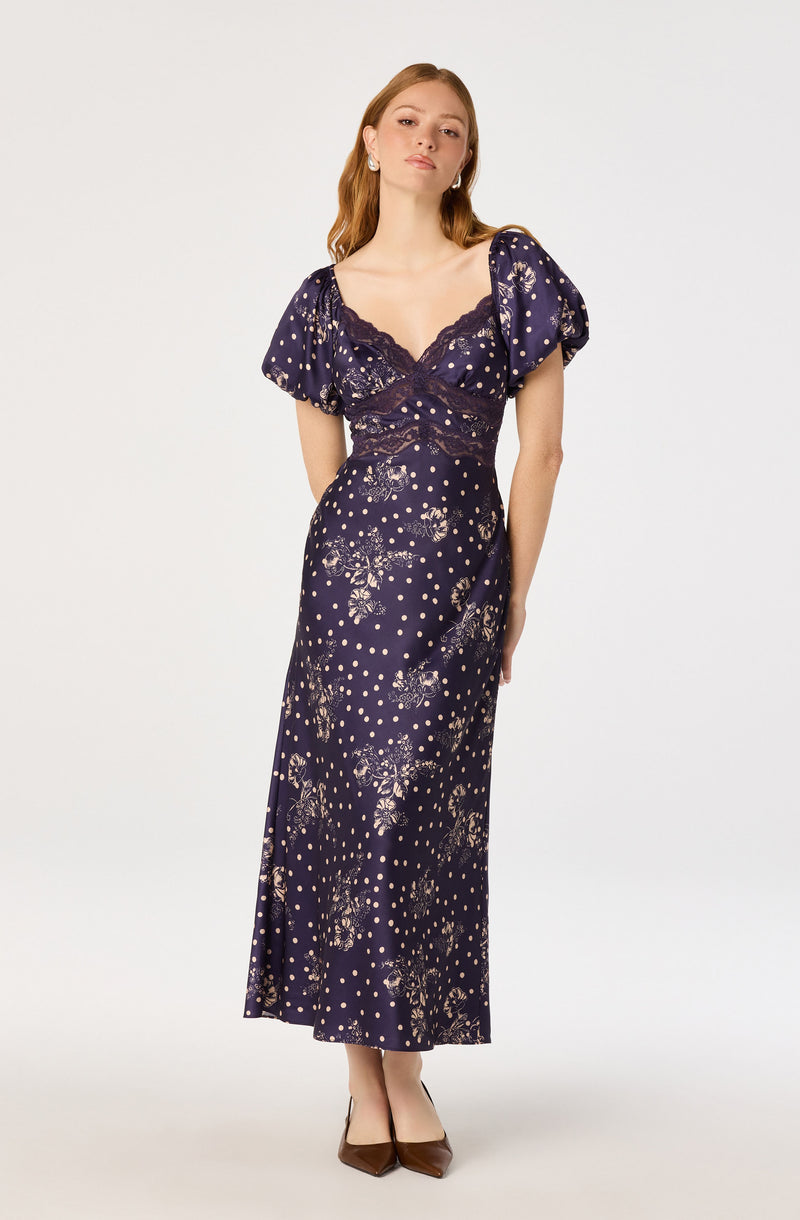 Woman in a navy blue dress with puffed short sleeves, floral and polka dot pattern, and lace detailing.