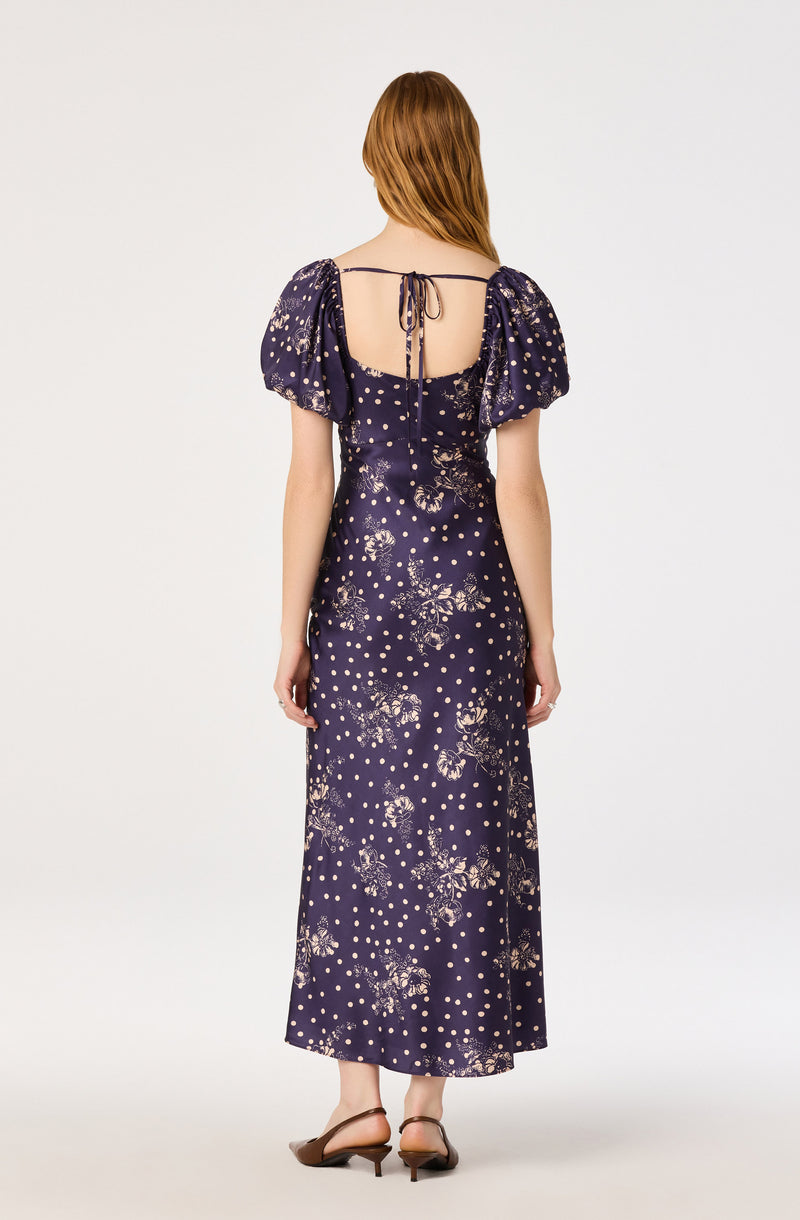 Woman wearing a navy blue floral and polka dot maxi dress with puff sleeves and an open back.