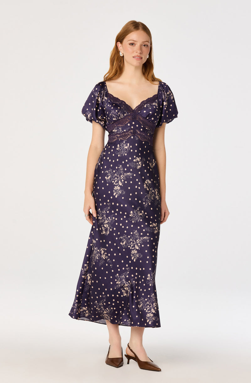 Woman wearing a navy blue dress with lace bodice, puff sleeves, and floral polka dot pattern.