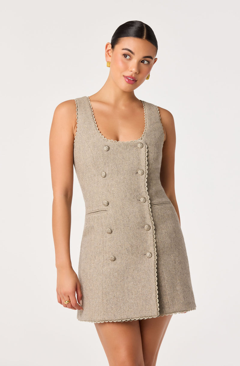 Model wearing a beige sleeveless dress with scalloped edges and decorative buttons.