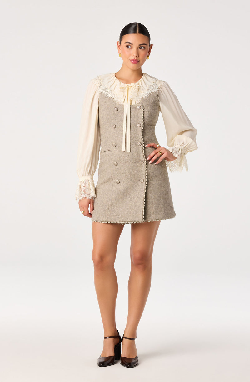 Woman wearing a beige and gray vintage-inspired dress with lace details and puffed sleeves.