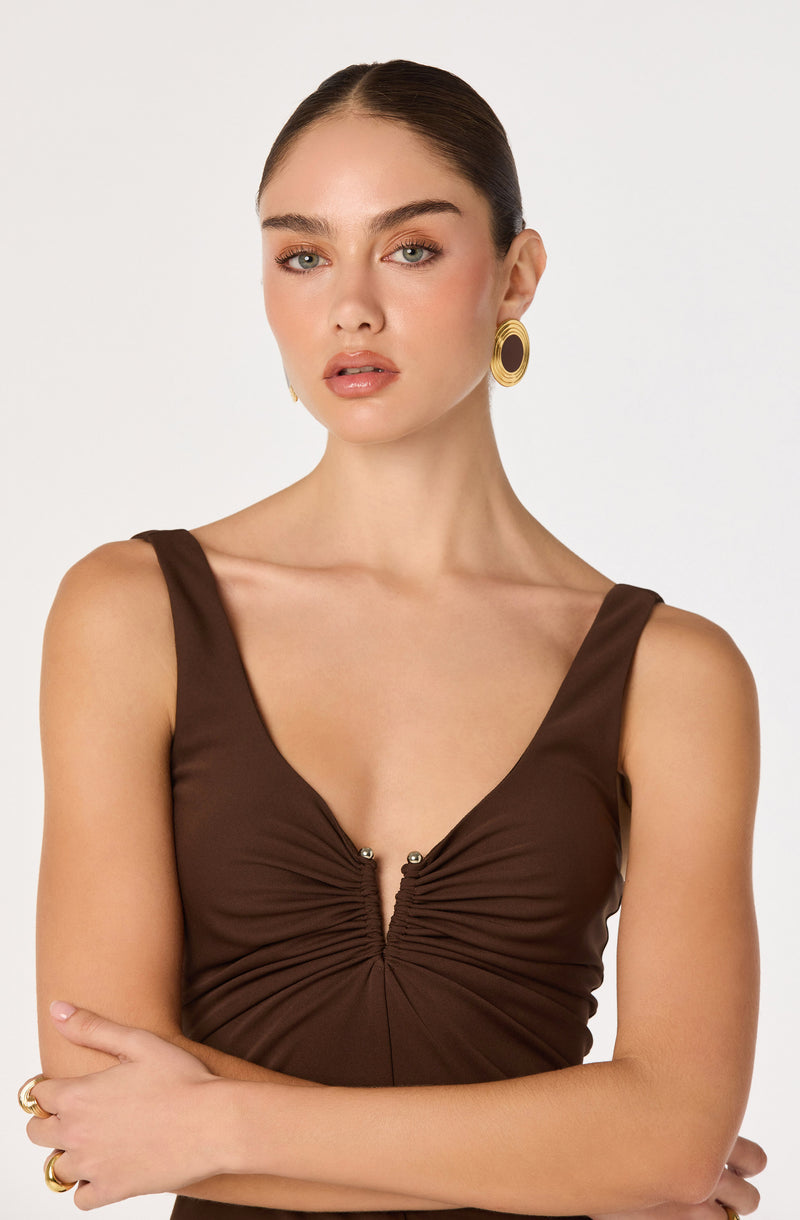 Girl in a sleeveless, brown dress with a ruched center and gold hoop earrings.