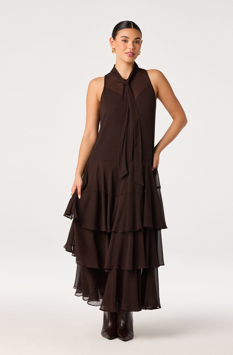 Woman wearing a sleeveless, dark brown tiered dress with a tie detail at the neck.