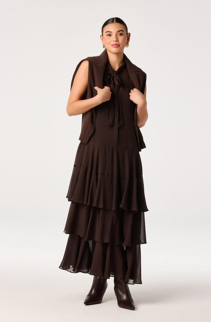 Woman in a tiered brown dress with ruffled layers, paired with dark brown boots and a sleeveless brown vest.
