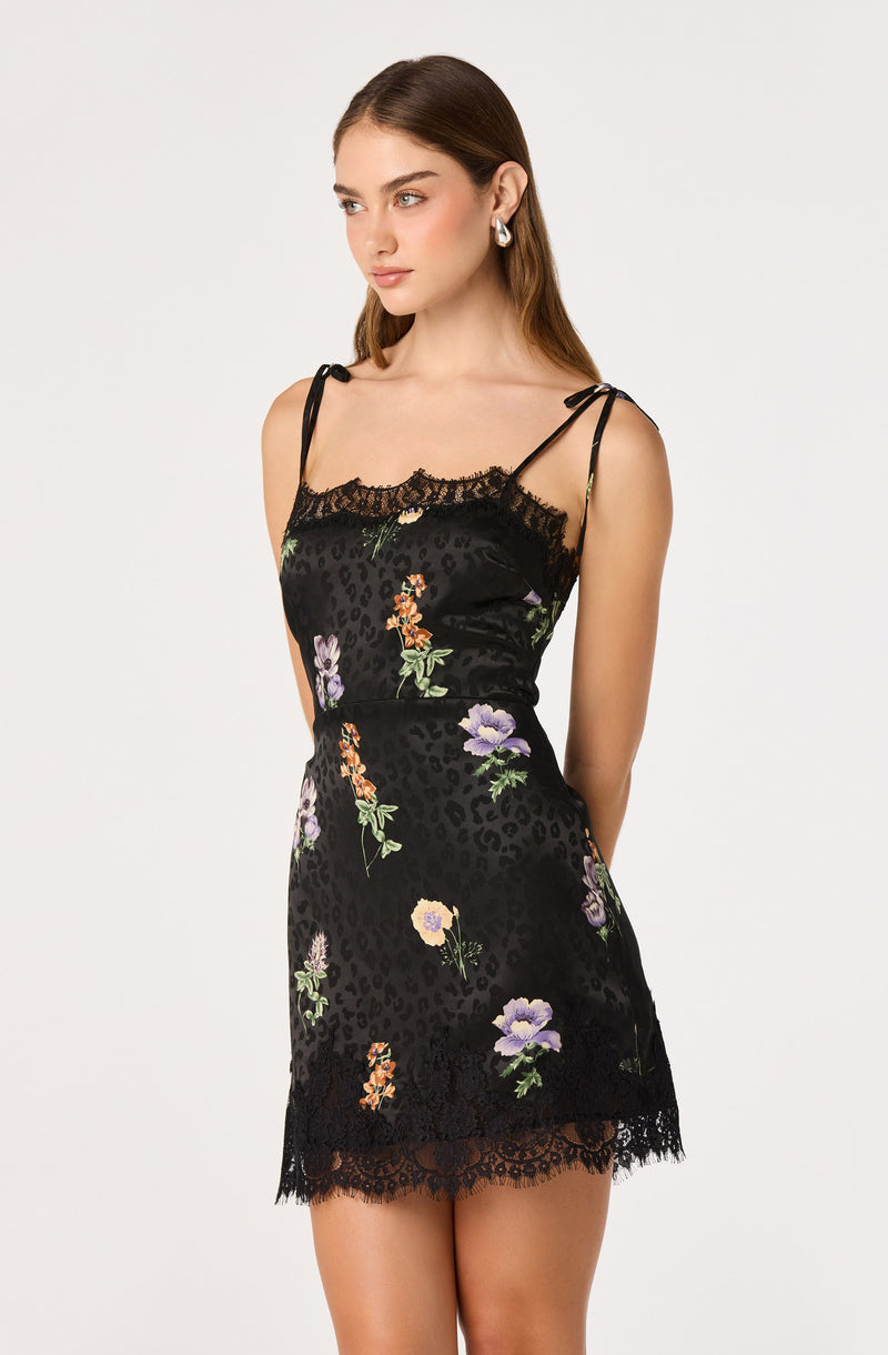 Woman in a black floral slip dress with lace trim and spaghetti straps.