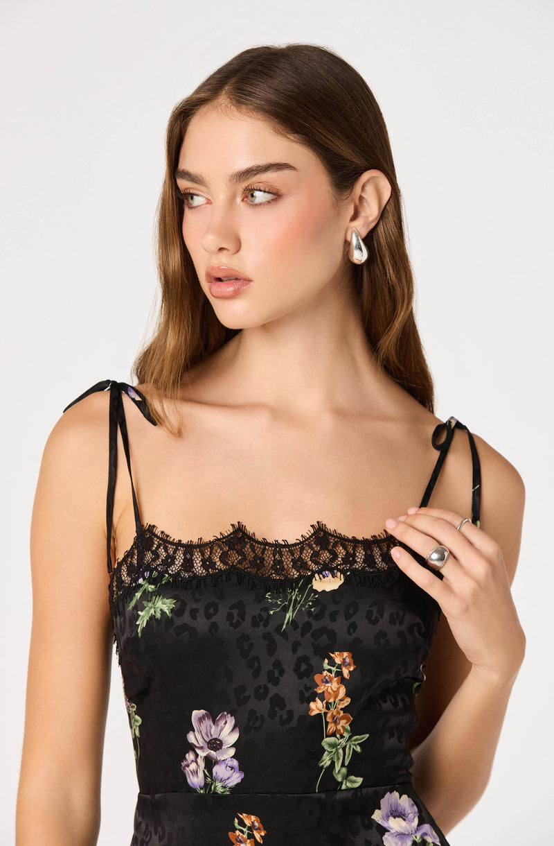 Woman in a black floral dress with lace trim and thin shoulder straps.