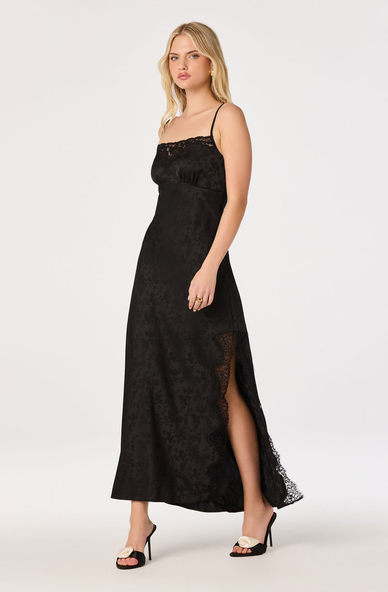Woman in a long black dress with spaghetti straps and lace detail at the top and along the side slit.
