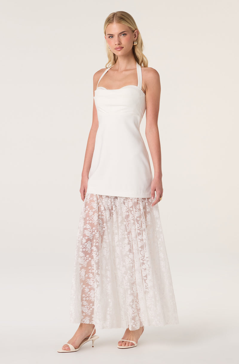 Woman wearing a white sleeveless top with thin straps and a sheer lace skirt.