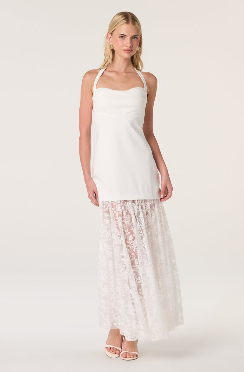 Woman wearing a white tank top and a long white lace skirt with sheer floral pattern.