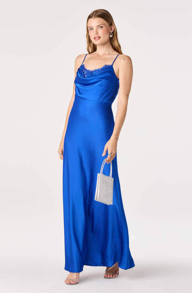 Woman in a long, shiny royal blue dress with lace trim, thin straps, holding a small silver clutch.