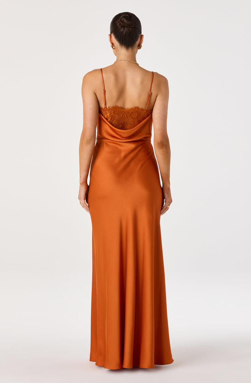 Back view of a woman in a long, satin, burnt orange slip dress with lace detail at the bust.