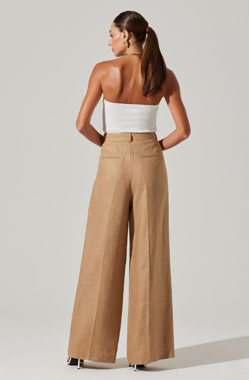 A woman is wearing a white, strapless, textured top paired with high-waisted, wide-leg beige trousers.