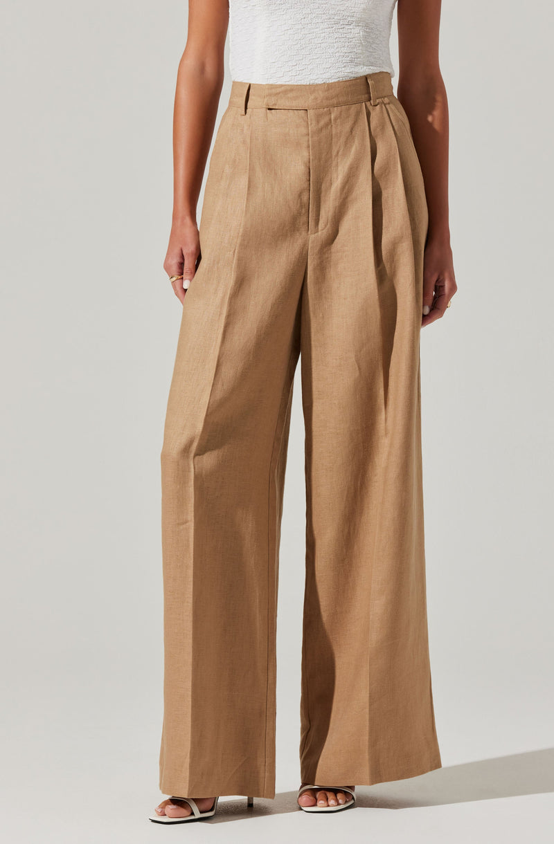A person is wearing high-waisted, wide-leg beige trousers with a pleated front and a belt loop. The trousers have a crisp, tailored appearance with a smooth finish. They are paired with a sleeveless white textured top.