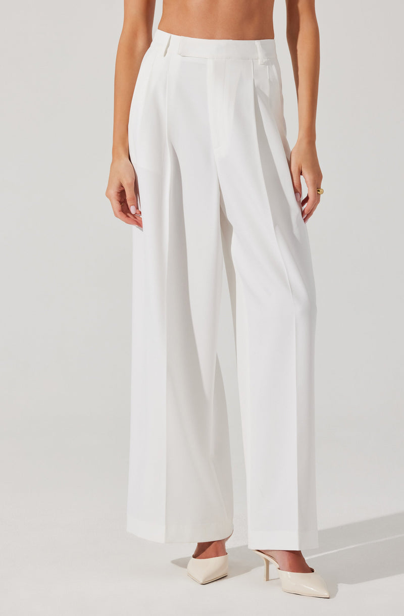 A person is wearing high-waisted, wide-leg white trousers with belt loops and pleats in the front. They are paired with pointed-toe white heels.