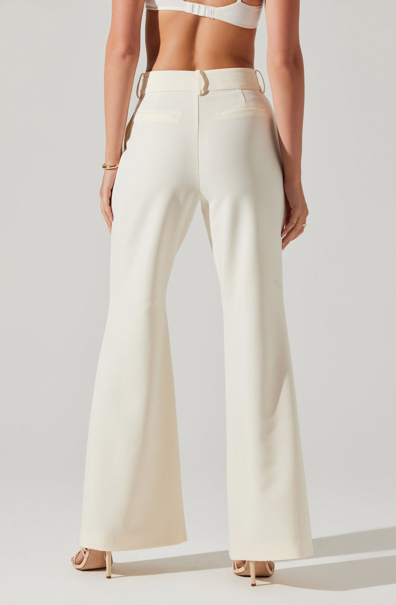 The image shows a person wearing high-waisted, wide-leg cream-colored trousers with belt loops, positioned against a plain light background. The person is also wearing a matching cream-colored cropped top and nude-colored heels.