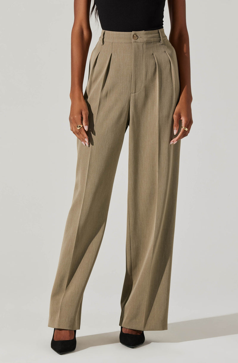 A person is wearing high-waisted, beige wide-leg dress pants with pleats at the waist. The pants feature belt loops, a button closure, and long, loose-fitting legs that extend down to the floor, covering the shoes. The individual is also wearing a sleeveless black top.