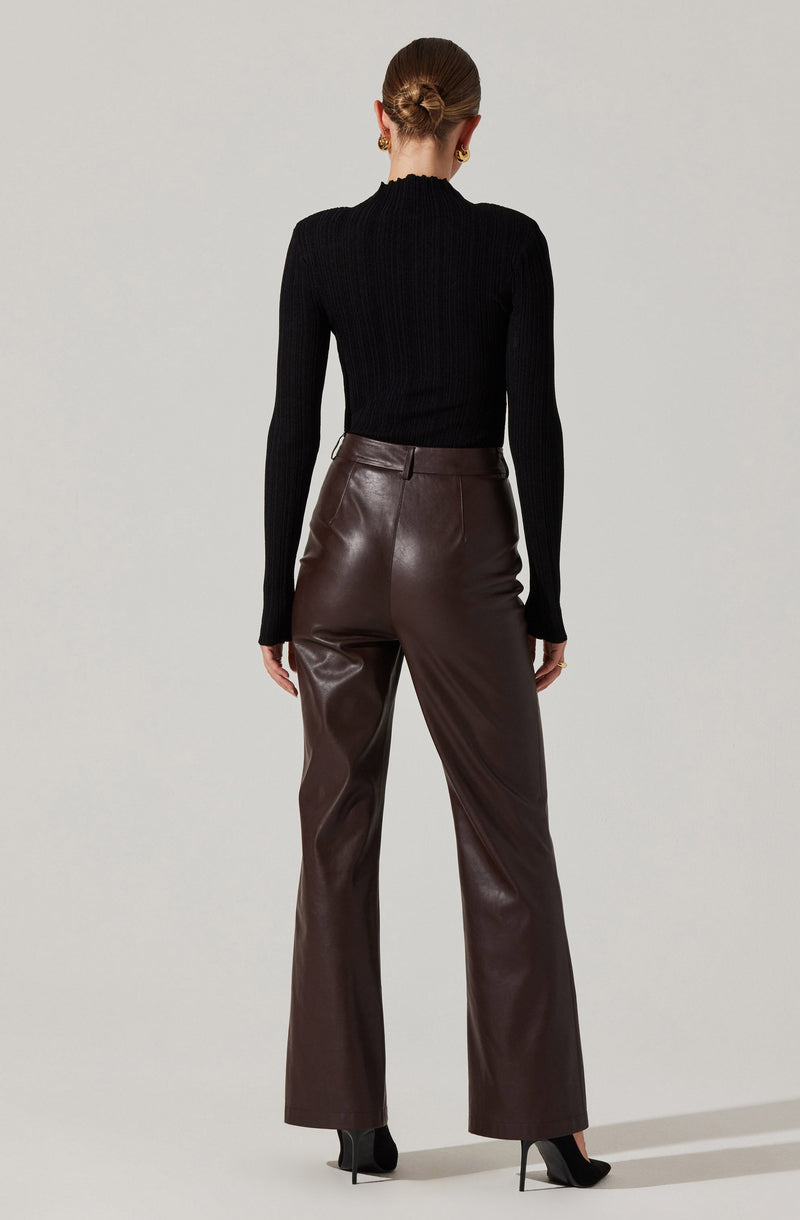 A person is wearing a fitted, long-sleeve, ribbed black sweater with a high neckline. They are also wearing high-waisted, dark brown leather pants with a straight-leg cut, paired with black high-heeled shoes.