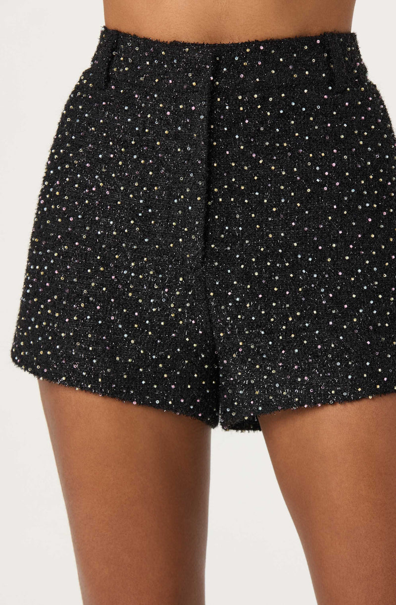 A pair of high-waisted black shorts covered in multicolored glittering dots, giving a sparkly and festive appearance. The shorts have a fitted waistband and a slightly loose fit through the legs.