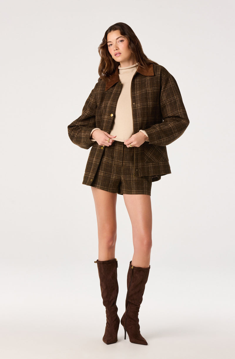 Brown plaid blazer, matching shorts, beige turtleneck, and tall brown boots.