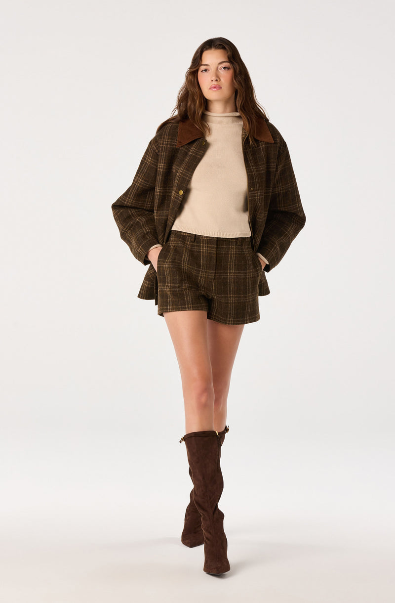 Woman wearing brown plaid jacket, matching shorts, beige sweater, and brown knee-high boots.