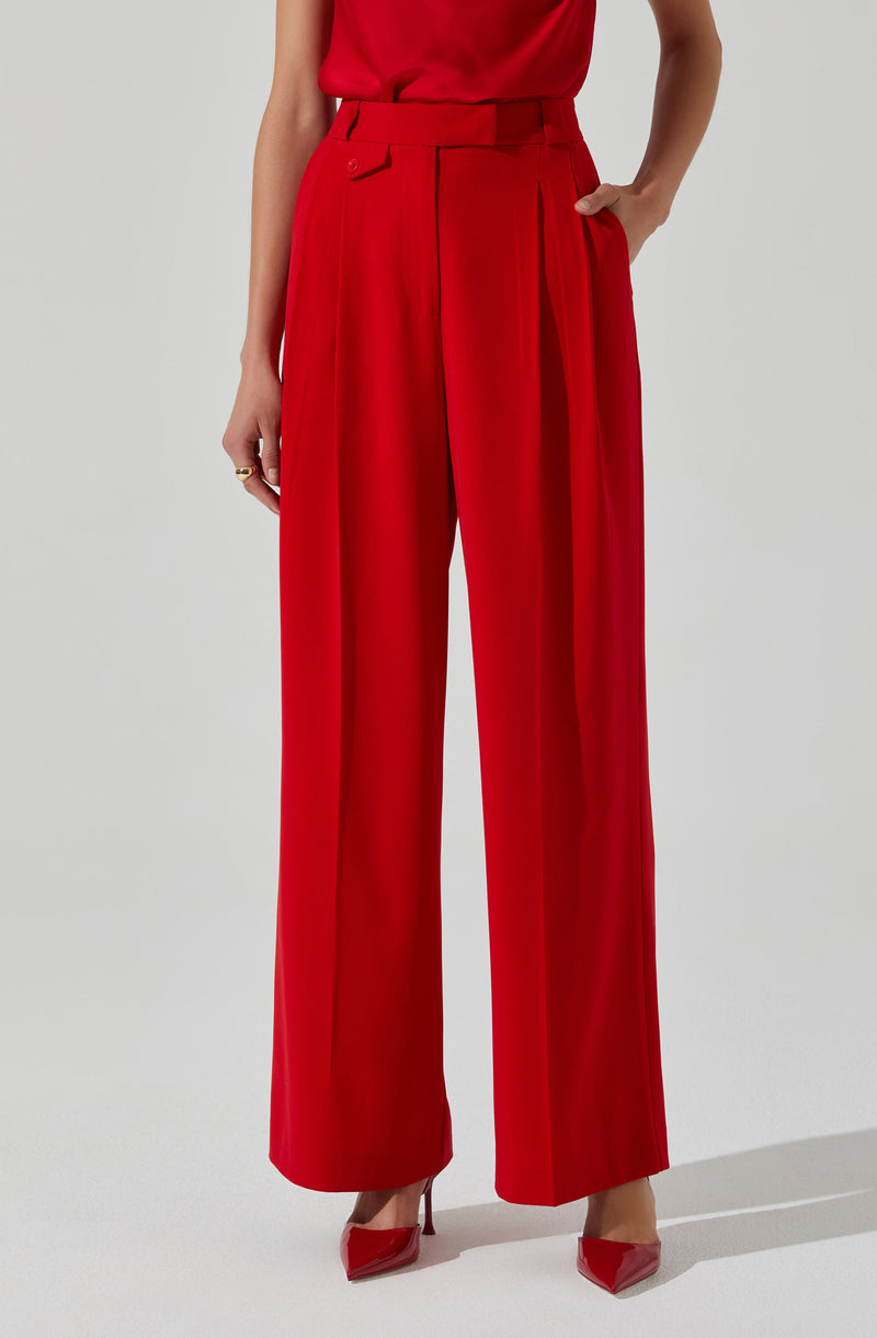 The image shows a person wearing high-waisted, wide-leg red trousers with pleats running down the front, paired with a sleeveless red top. They are also wearing red pointed-toe high heels.
