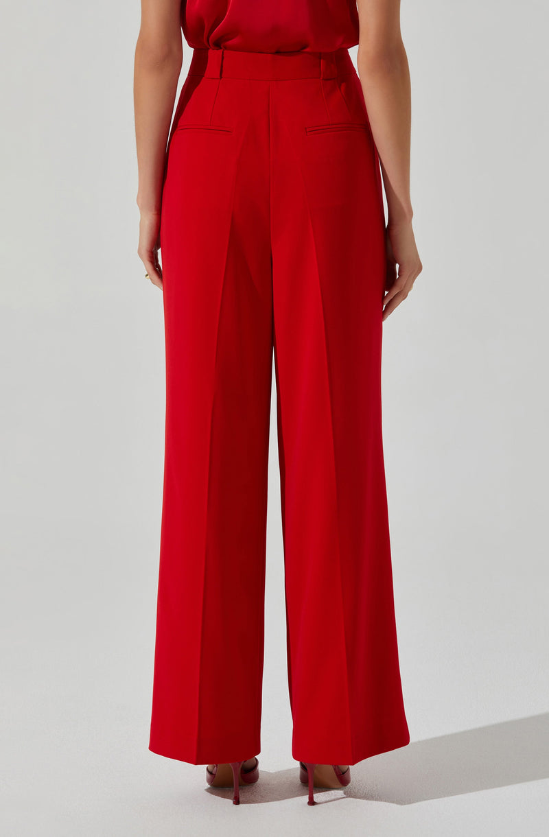 The image shows a person wearing high-waisted, wide-leg red trousers with a tailored fit. The trousers feature a front seam detail, a waistband with belt loops, and slit pockets on the back. The person is also wearing a sleeveless, loose-fitting red top tucked into the trousers. The overall look is elegant and sophisticated, with the bright red color making a bold statement.