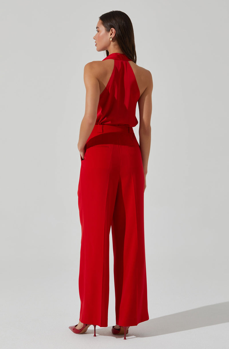 A woman is wearing a sleeveless red halter neck top with a keyhole detail at the back, paired with high-waisted red wide-leg trousers. She completes the look with nude high heels.