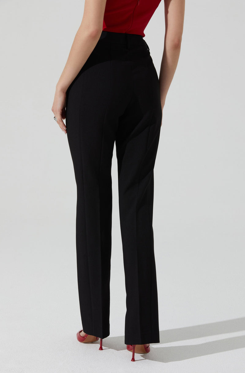 A person is wearing black tailored pants with a high waist and a front creased design. They are also wearing a sleeveless red top. The pants have a classic, straight-leg fit and are paired with red high-heeled shoes.
