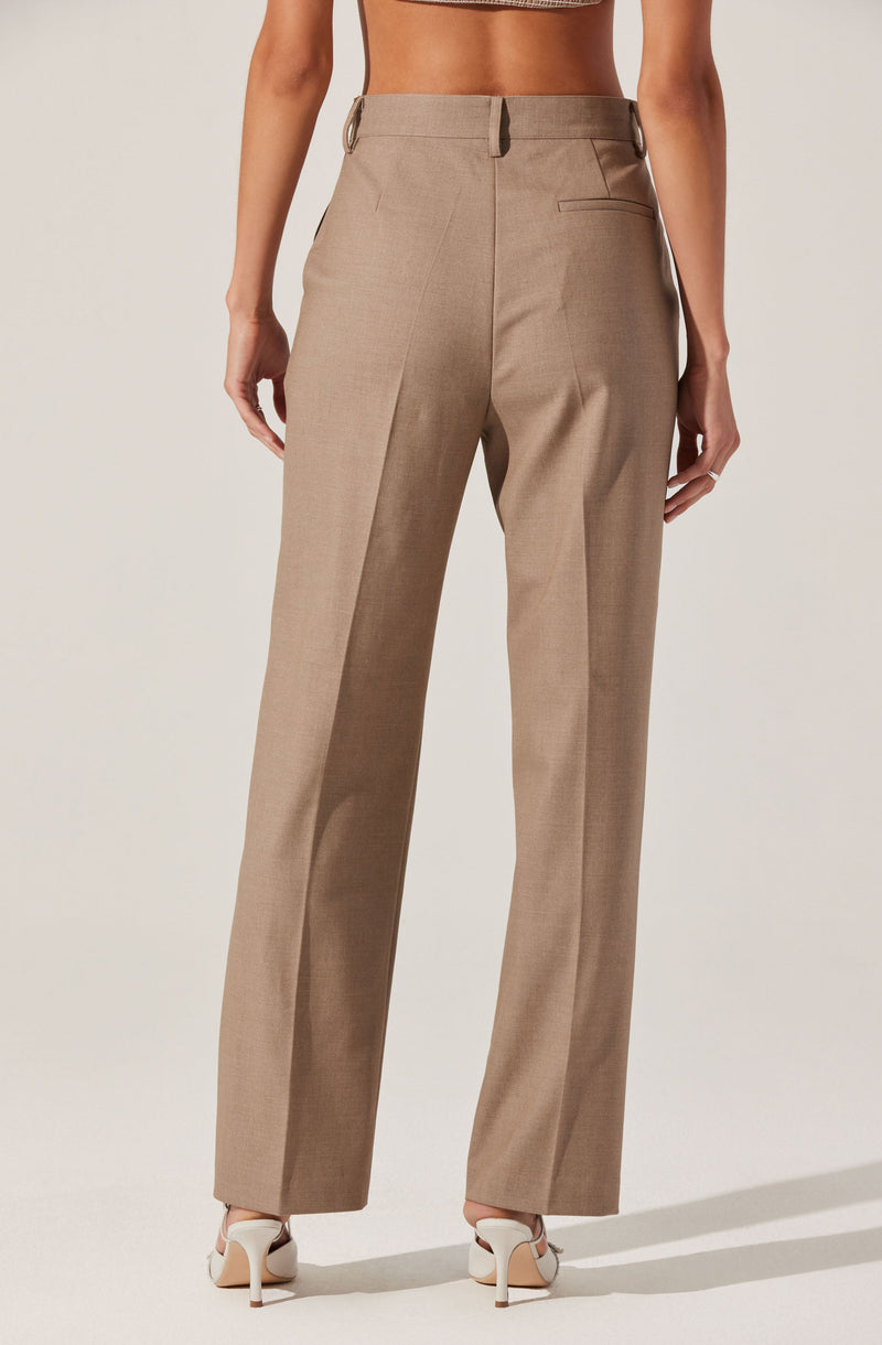 A person is wearing beige, high-waisted, wide-leg dress pants with a tailored fit. The pants have belt loops at the waistband, a single back welt pocket, and a subtle pleat detail running down the front of each leg. The person is also wearing white high-heeled shoes.