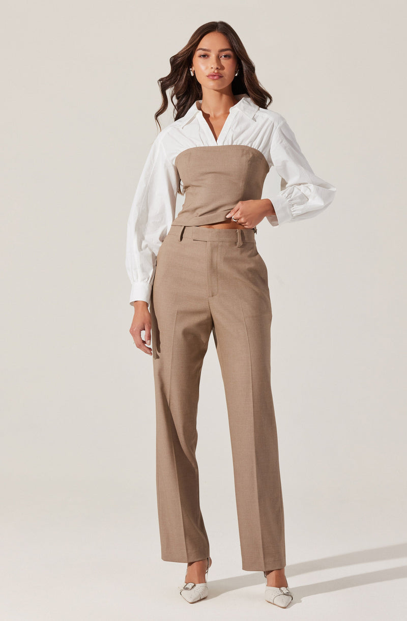 A woman is wearing a white long-sleeve button-up shirt with puffed sleeves, paired with a strapless beige top worn over the shirt. She also has on beige high-waisted, straight-leg trousers with a front crease. She completes the look with white pointed-toe shoes.