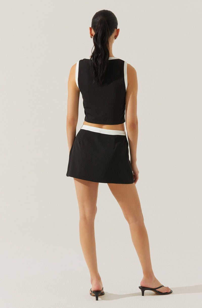 A woman is wearing a sleeveless, sporty black top with white trim around the armholes and neckline. She has a matching black skirt with a white waistband. She is also wearing black open-toe, heeled sandals. Her hair is styled in a long, smooth ponytail.