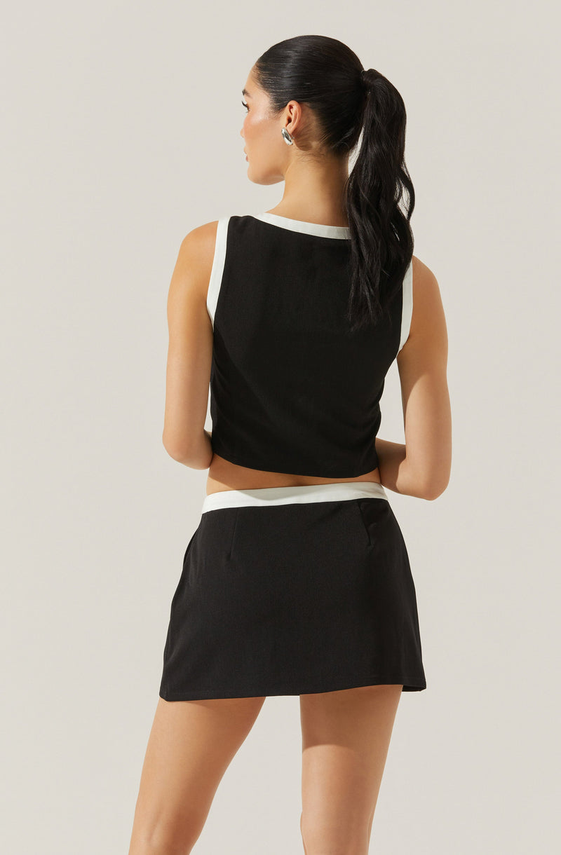 A woman is wearing a sleeveless black crop top with white trim around the armholes and neckline, paired with a matching black skirt that has a white waistband.