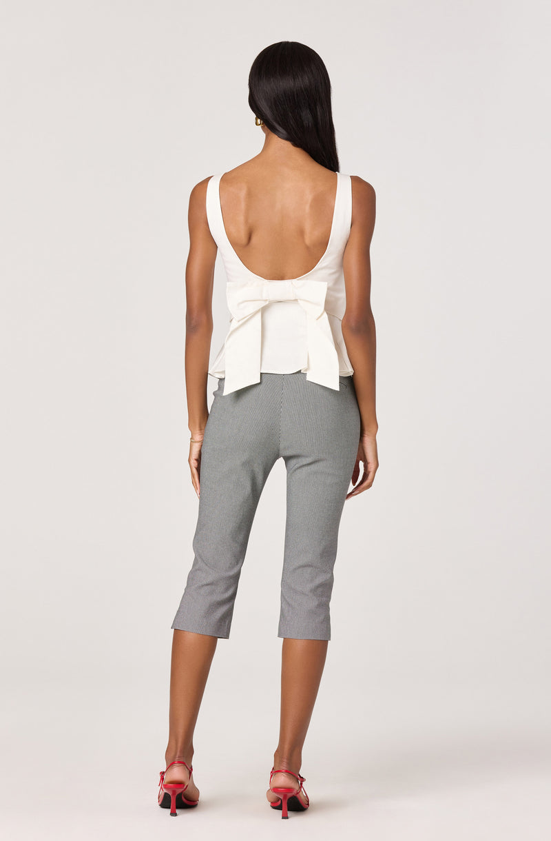 Woman wearing a white sleeveless top with a large bow at the back and gray cropped pants.