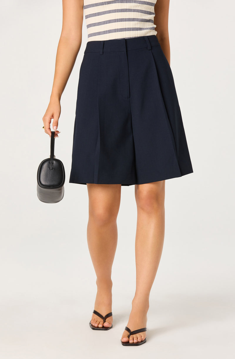 Woman wearing a striped sleeveless top and high-waisted navy blue A-line skirt, holding a black handbag, and wearing black sandals.