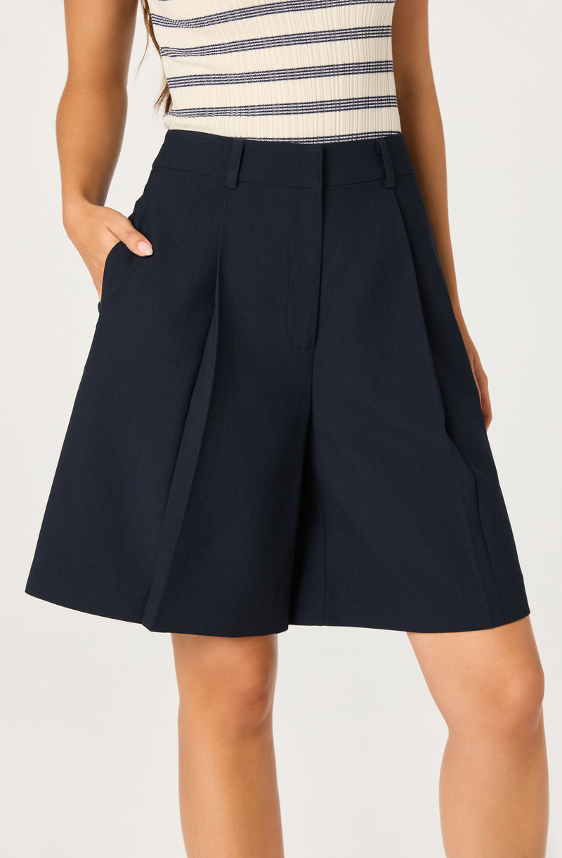 Woman wearing navy wide-leg shorts with pleats and a striped sleeveless top.