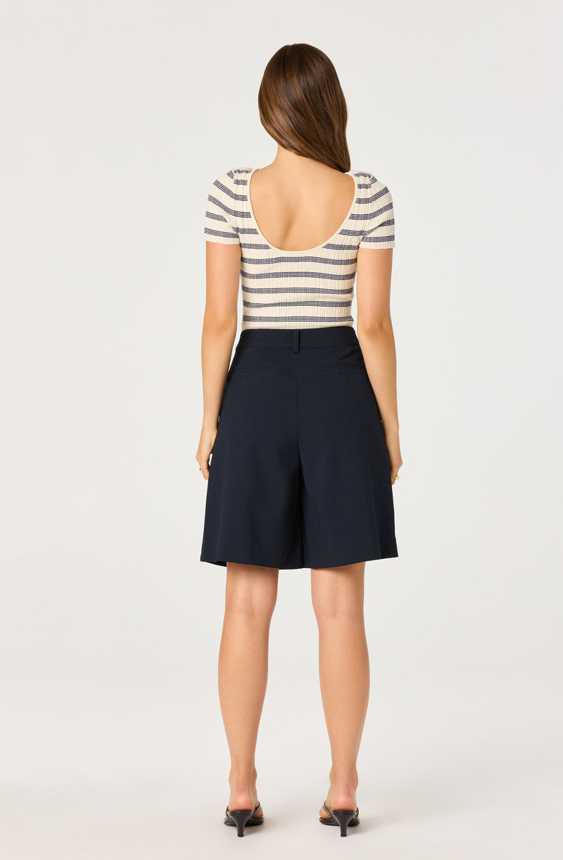Woman wearing a striped short-sleeve top and high-waisted navy shorts, seen from the back.